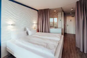 Doppelzimmer Bett mit weißen Laken und einem Vorhang im Hintergrund.