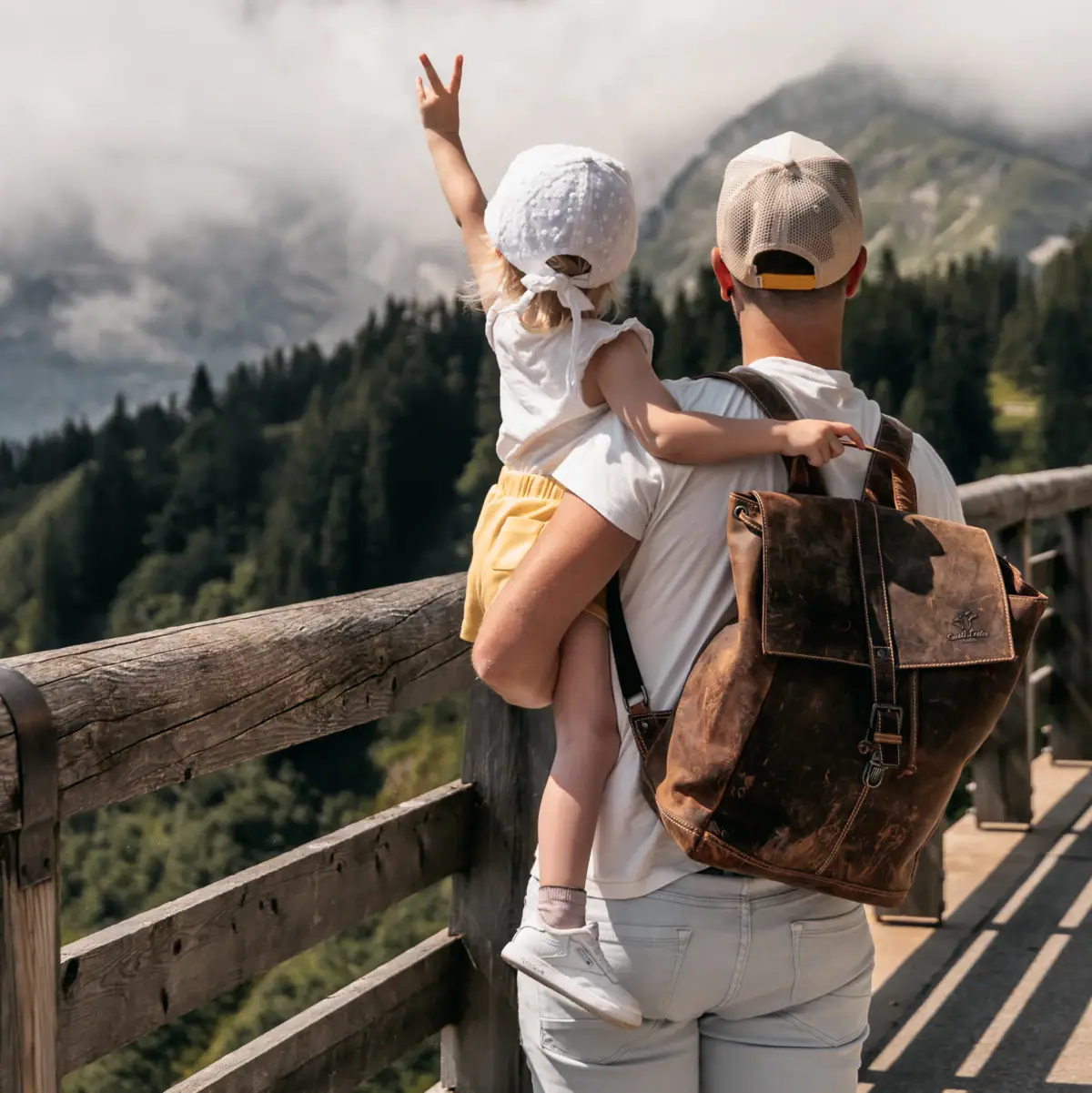 Panoramastraße Ein Mann und ein Kind stehen auf einem Holzgeländer und blicken auf Berge.