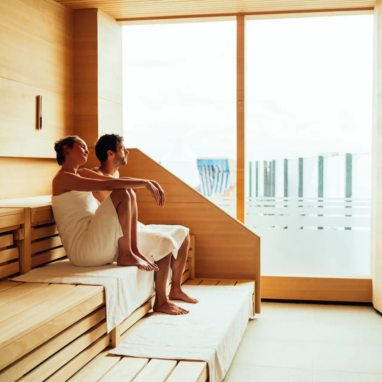 Sauna mit Ausblick Ein Mann und eine Frau sitzen auf einer Bank in einer Sauna.