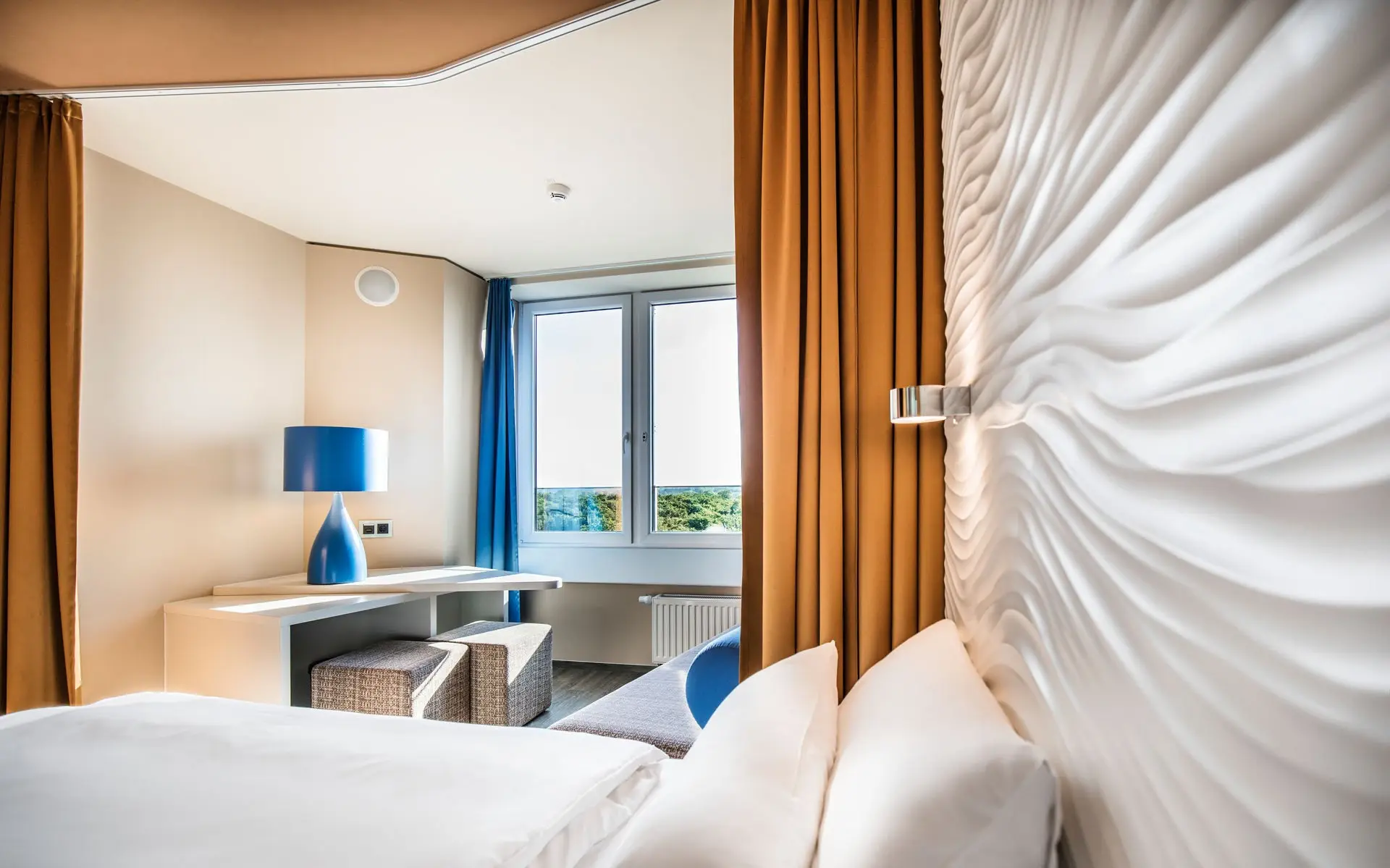 Ein Zimmer mit einem Bett und Schreibtisch, sowie einem großem Fenster