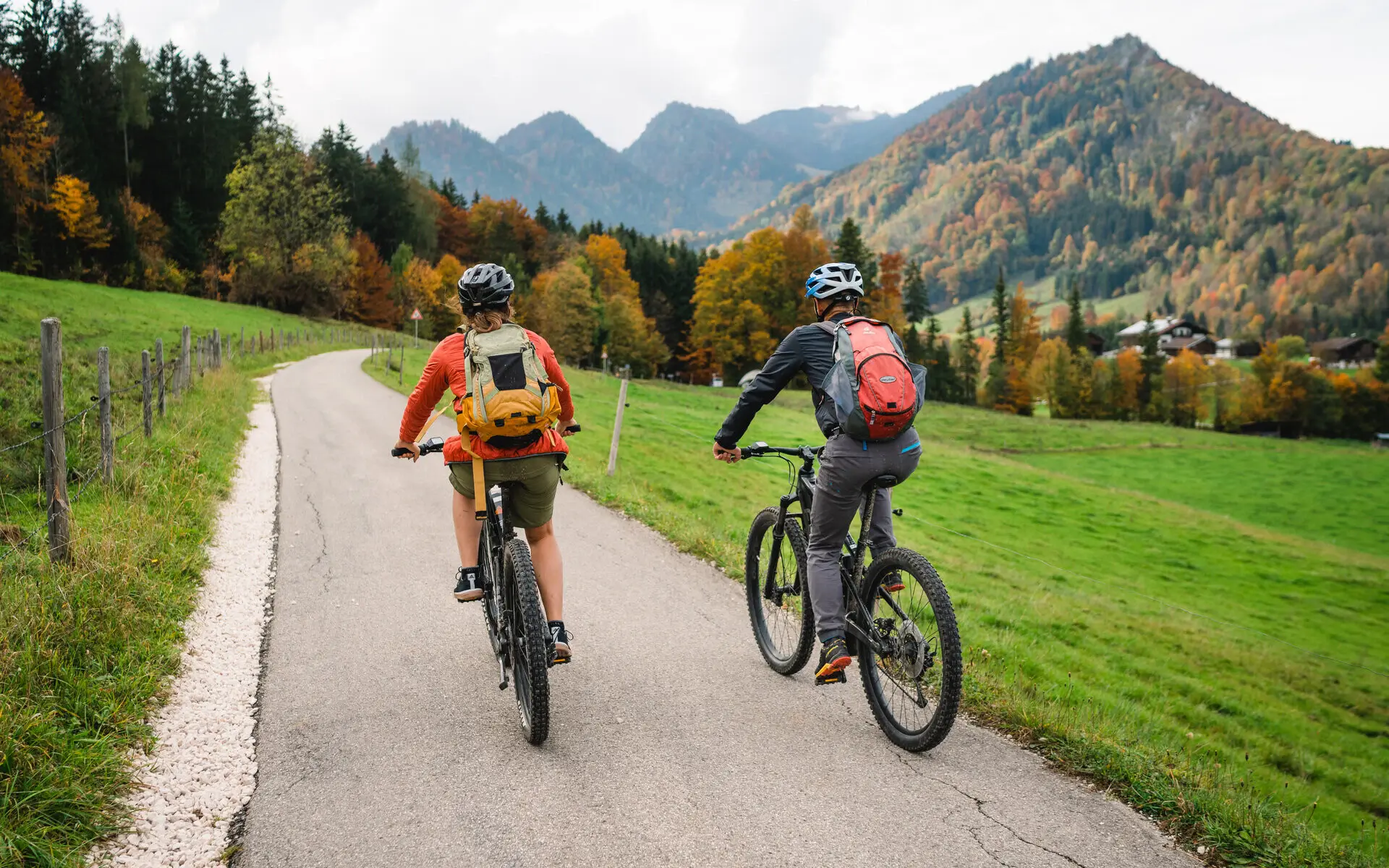 Zwei Personen fahren auf einer Straße Fahrrad und im Hintergrund sind Berge.