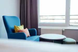 Sessel Blaues Sofa mit Kissen und rundem Tisch vor einem Fenster.