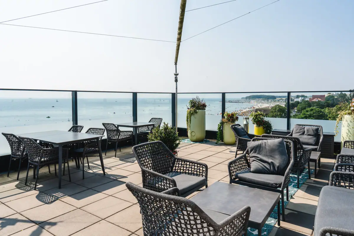 Terrasse aja Grömitz Eine Terrasse mit Stühlen und Tischen an einem sonnigen Tag und Blick auf die Ostsee.