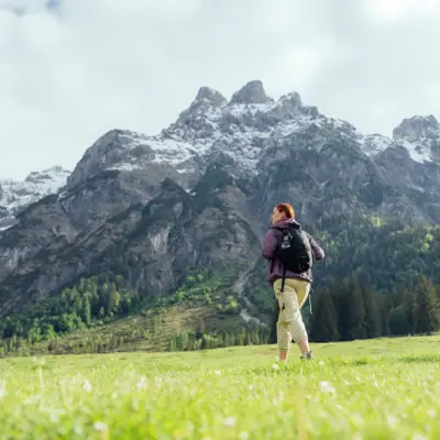Wandern Eine Frau steht in einem Feld mit Bergen im Hintergrund.