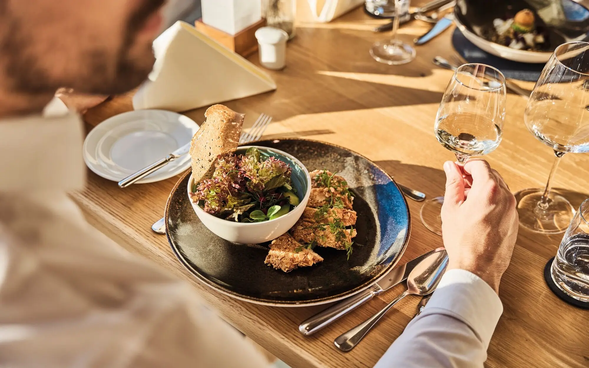 Restaurant Feinspitz Werfenweng Mann isst Salat und trinkt ein Glas Wein am Tisch.