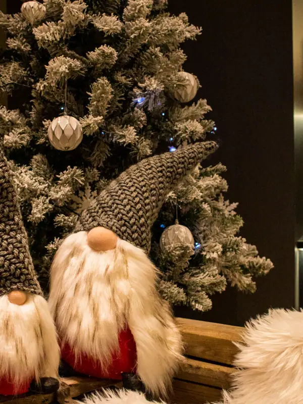 Weihnachtsdeko Zwei Wichtel sitzen auf einer Bank neben einem Weihnachtsbaum.