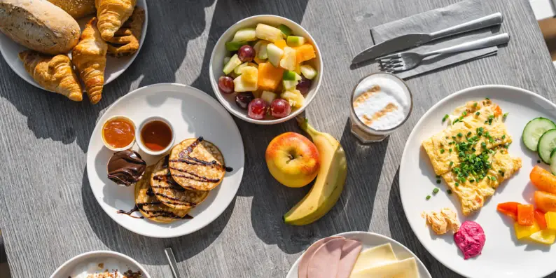 Ein von oben fotografierter Frühstückstisch, gedeckt mit Früchten, Pancakes und Brötchen. Ein von oben fotografierter Frühstückstisch, gedeckt mit Früchten, Pancakes und Brötchen.