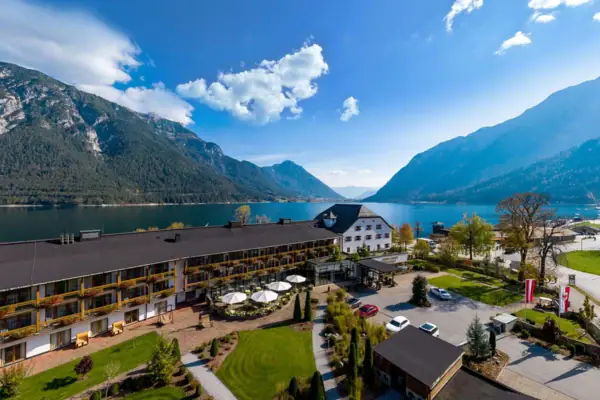 Ein Gebäude in der Nähe eines Sees mit Wolken am Himmel und Bäumen im Vordergrund.