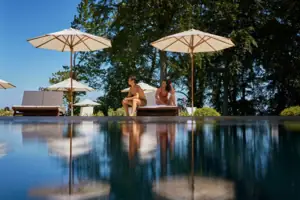 SPA Ein Mann und eine Frau sitzen am Poolrand mit Sonnenschirmen.