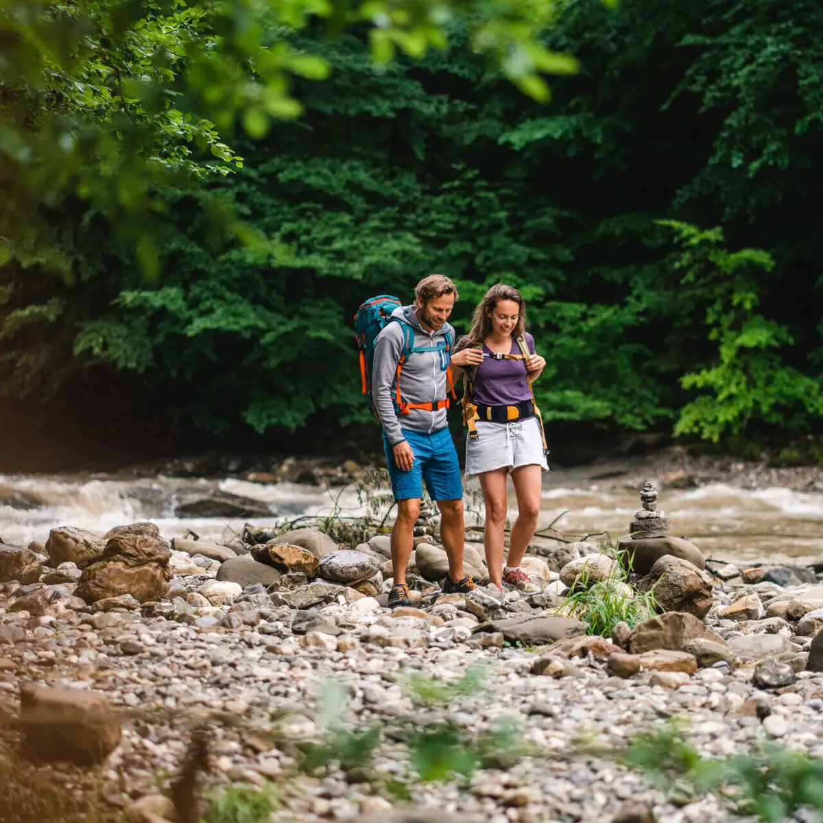Wandern im Flussbett Ein Mann und eine Frau stehen auf Felsen an einem Fluss.
