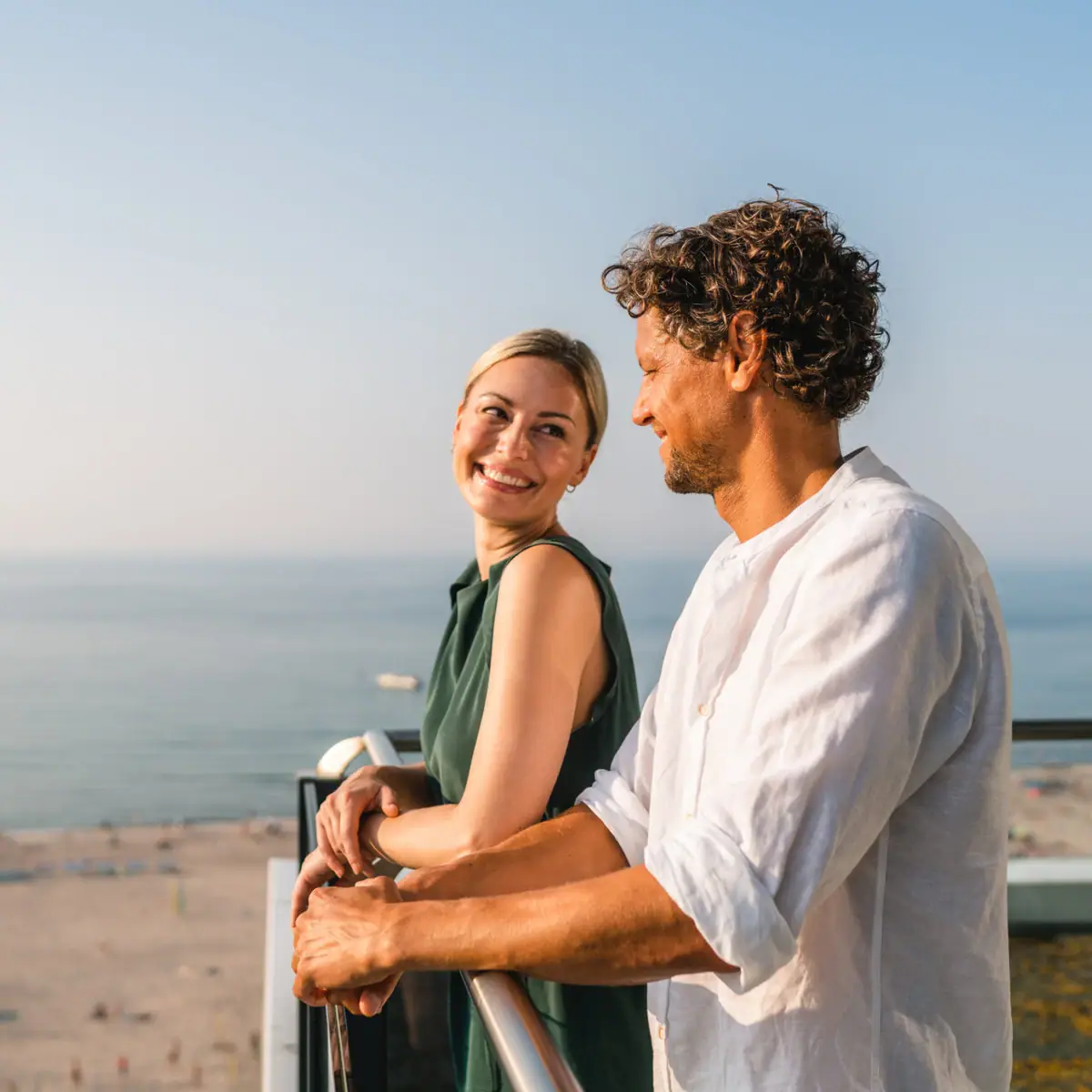 Ausblick vom Balkon Ein Mann und eine Frau stehen auf einem Balkon mit Blick auf einen Strand.