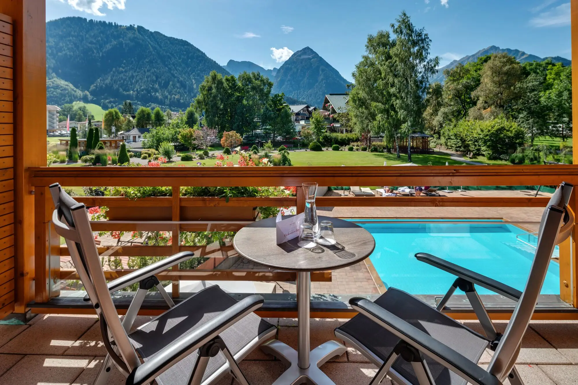 Zimmer mit Bergblick Ein Tisch und Stühle auf einem Balkon mit Blick auf einen Pool.