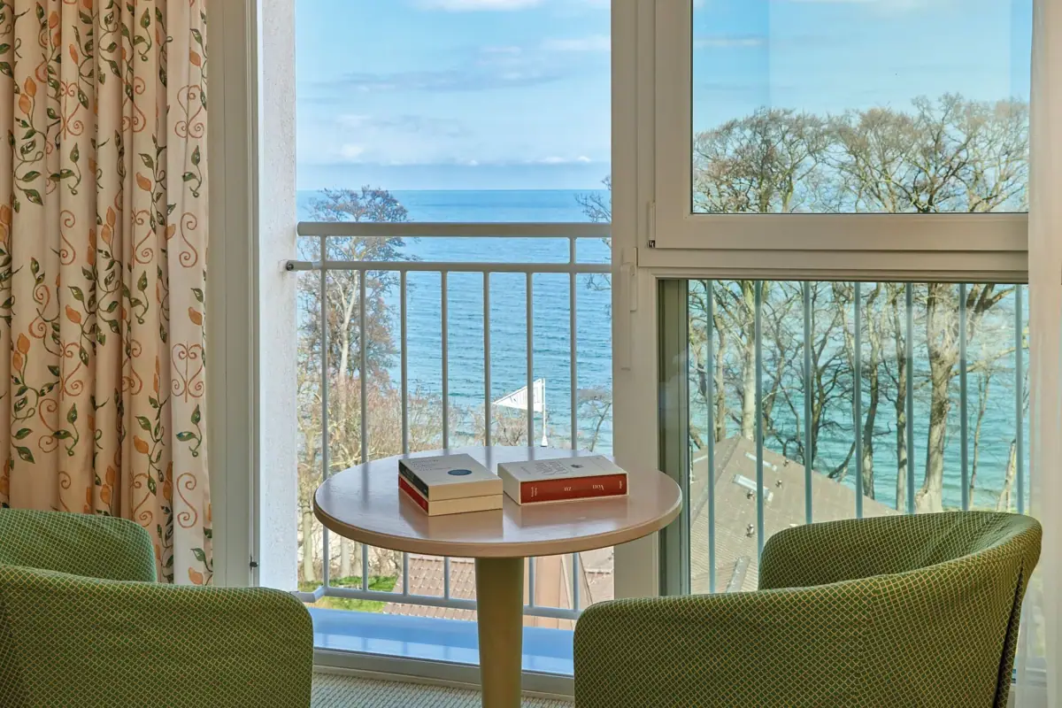 Ausblick Hotelzimmer Ein Tisch mit Büchern darauf, vor einem Balkon mit Blick auf den Ozean.