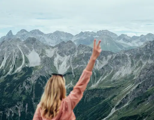 Aktiv mit aja Eine Frau steht auf einem Berg und hebt die Hand.