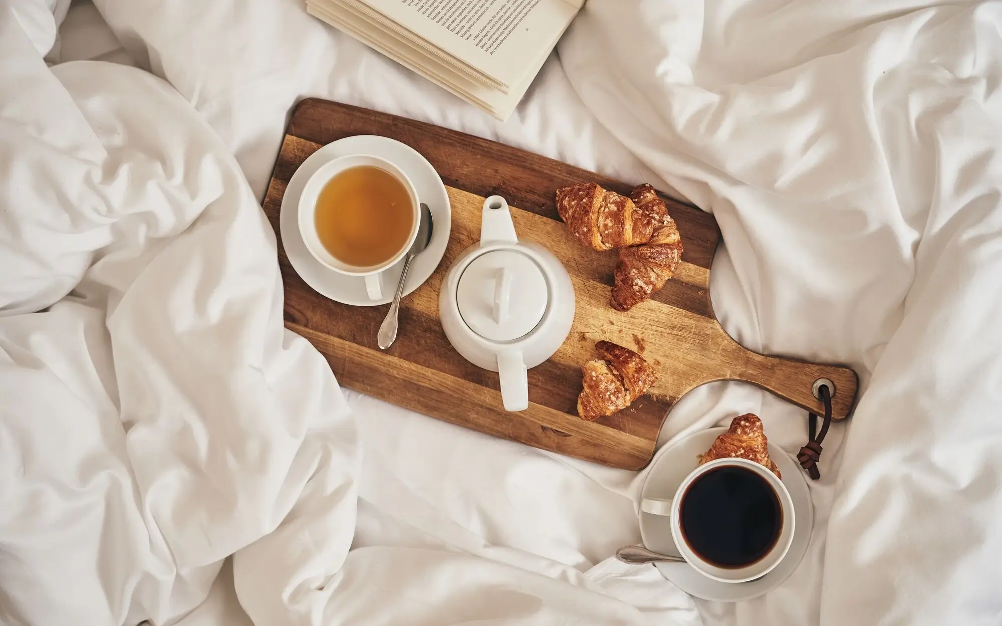 Tablett mit Tee und Croissants auf einem Bett.