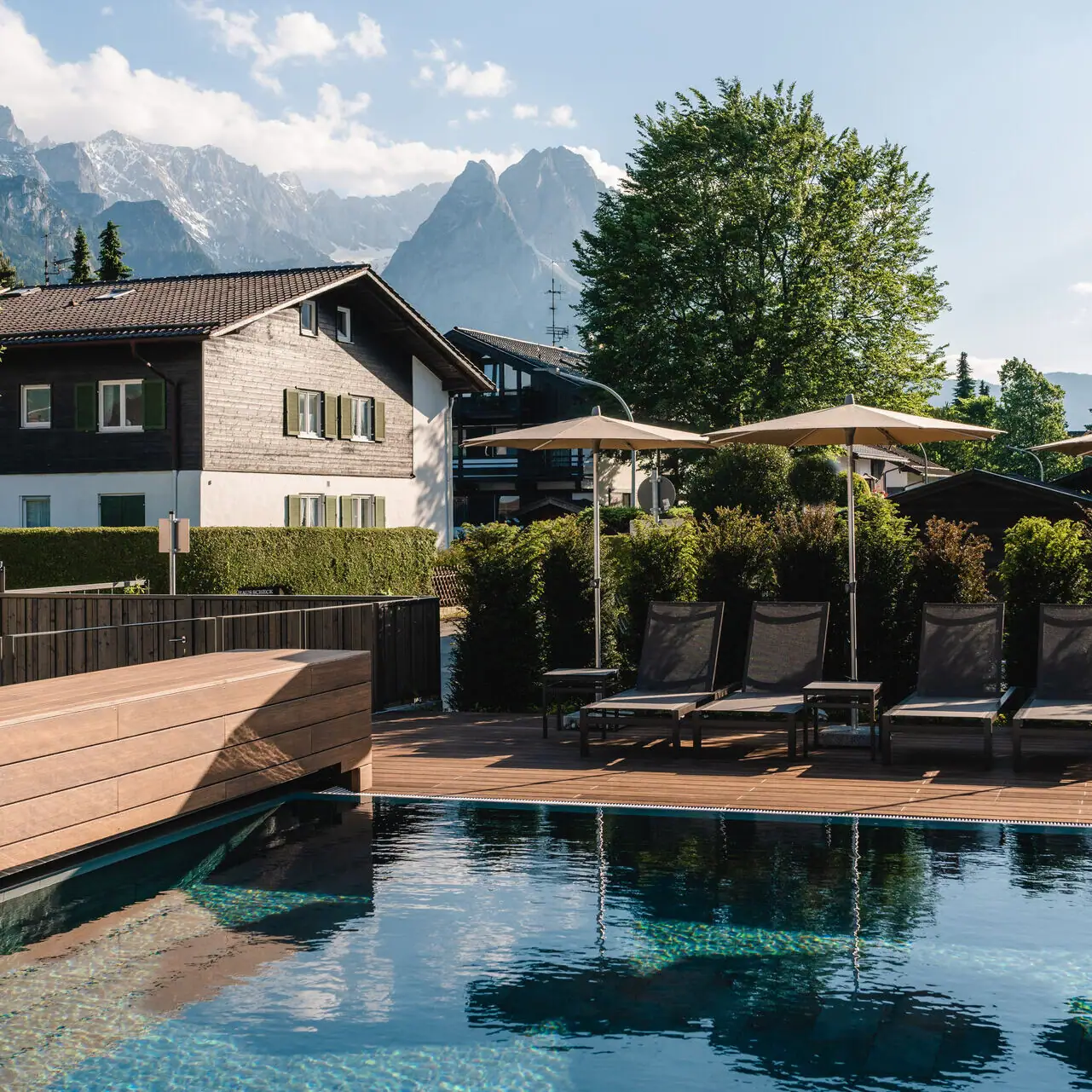 Außenpool aja Garmisch-Partenkirchen Ein Pool mit Stühlen und Sonnenschirmen neben einem Haus.