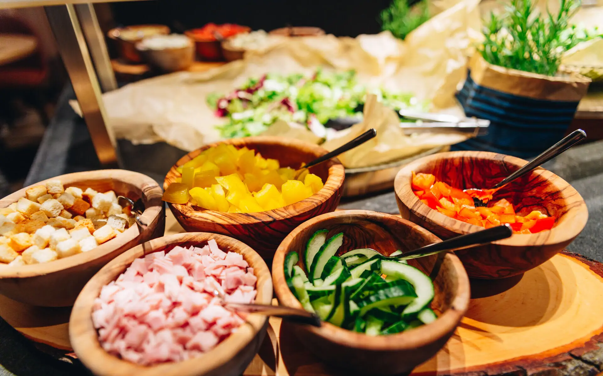 Salatbuffet Ein warm beleuchtetes Salatbuffet mit kleinen Holzschälchen, gefüllt mit verschiednen Salatzutaten.