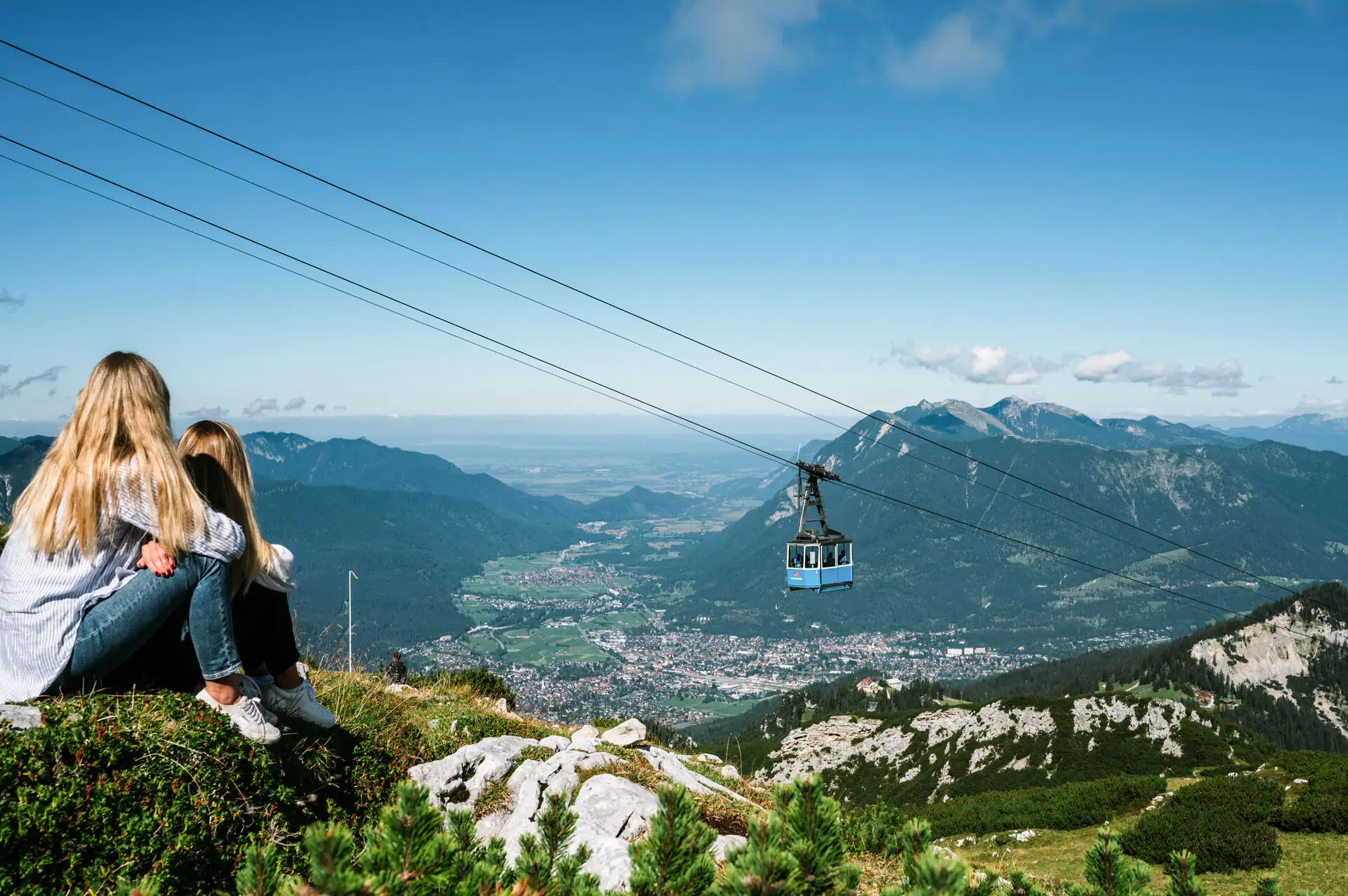 Zugspitze Ein Mädchen sitzt auf einem Berg und Blickt ins Tal, über ihr schwebt eine Seilbahn.