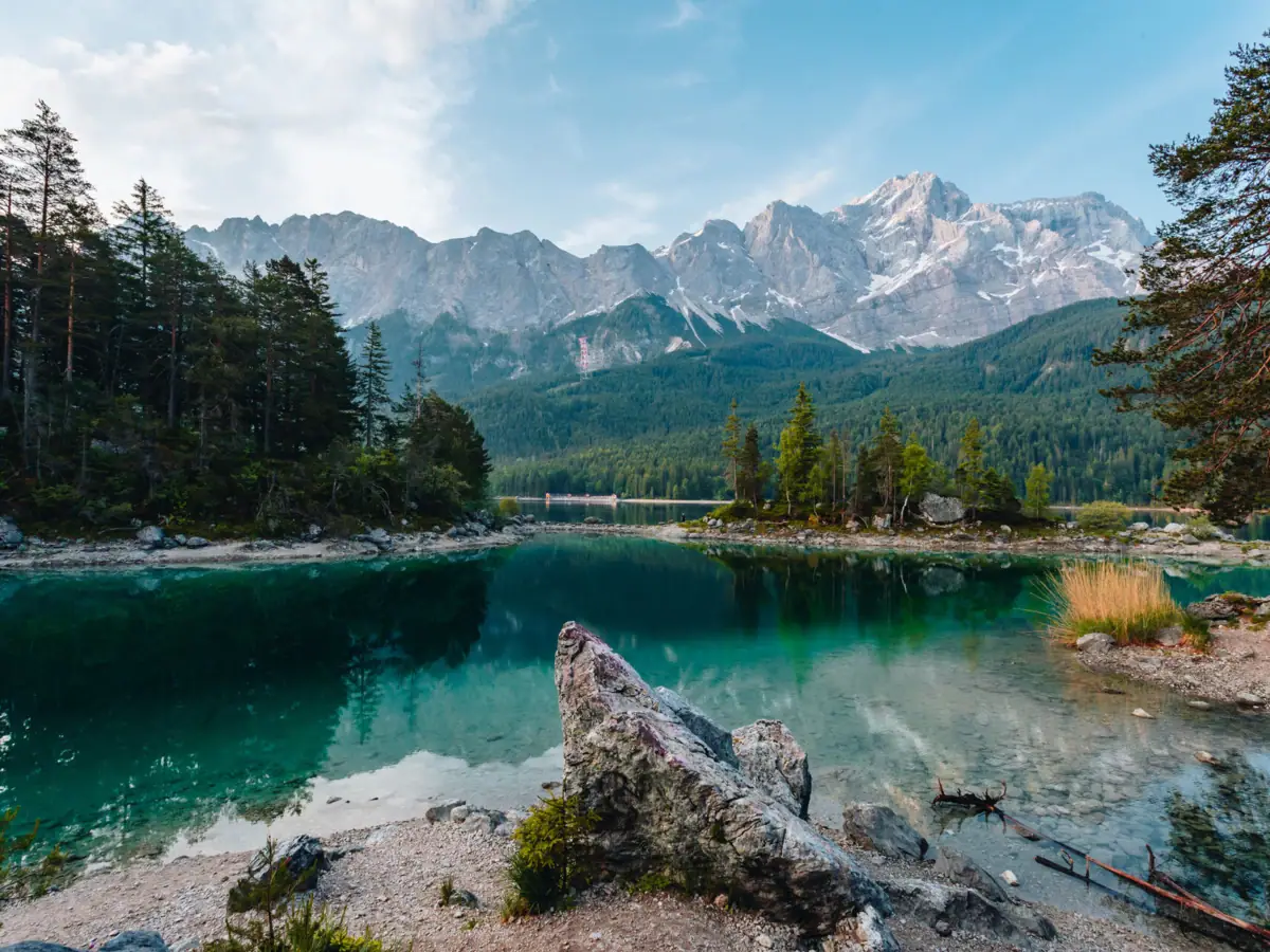 Der Eibsee Ein See mit Bäumen und Bergen im Hintergrund.