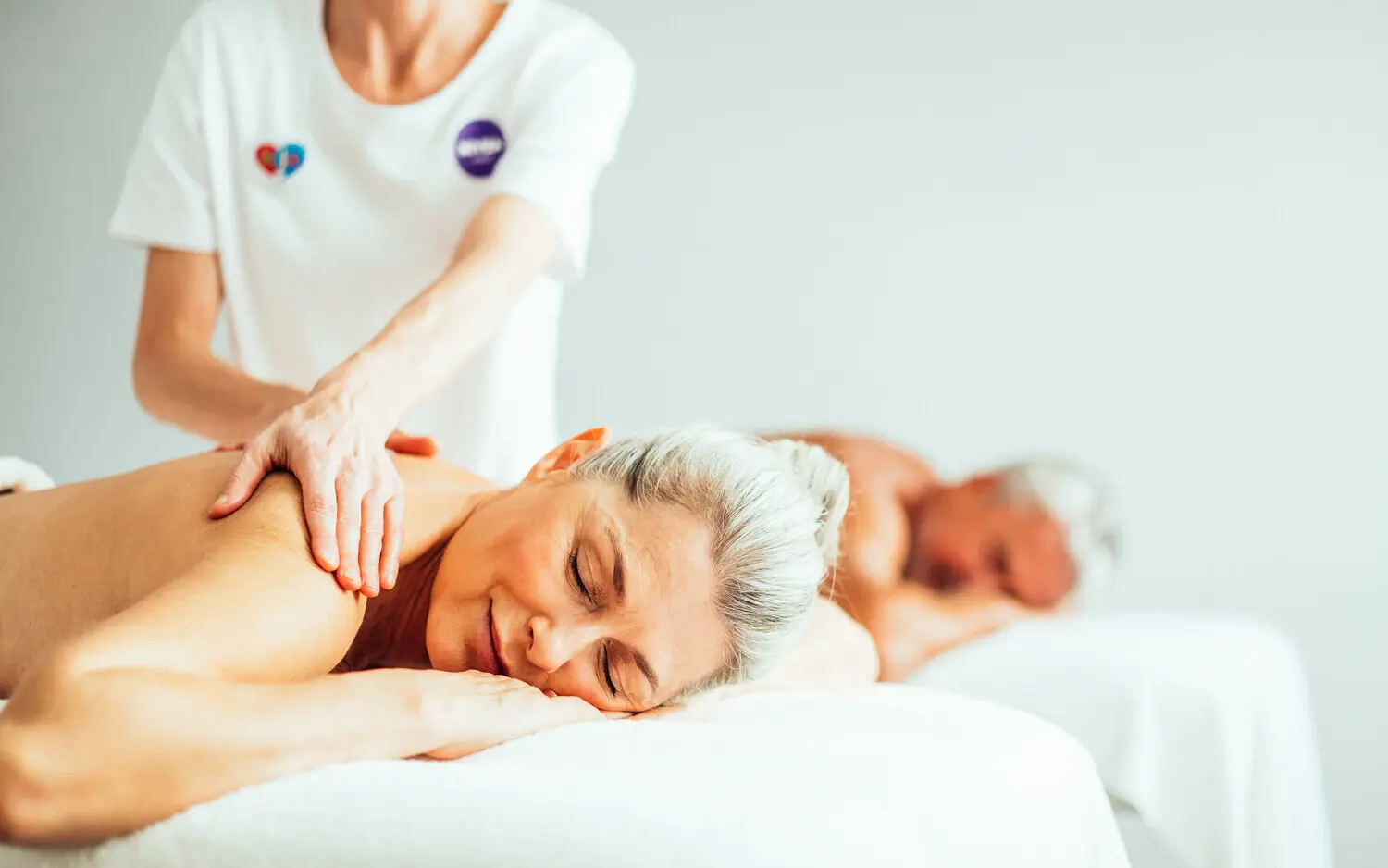 NIVEA Haus Bad Saarow Eine Frau liegt auf einer Massageliege und wird von einer Person am Rücken massiert. Im Hintergrund liegt ein Mann auf einer weiteren Liege und entspannt.