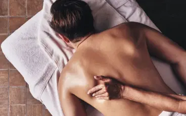 Eine Person liegt auf einem Handtuch mit dem Rücken nach oben und wird massiert.