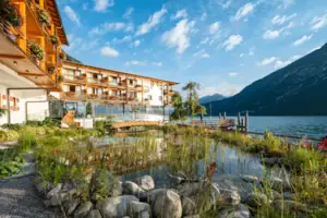 aja Fürstenhaus am Achensee Ein Gebäude vor einem Gewässer mit Bergen im Hintergrund.