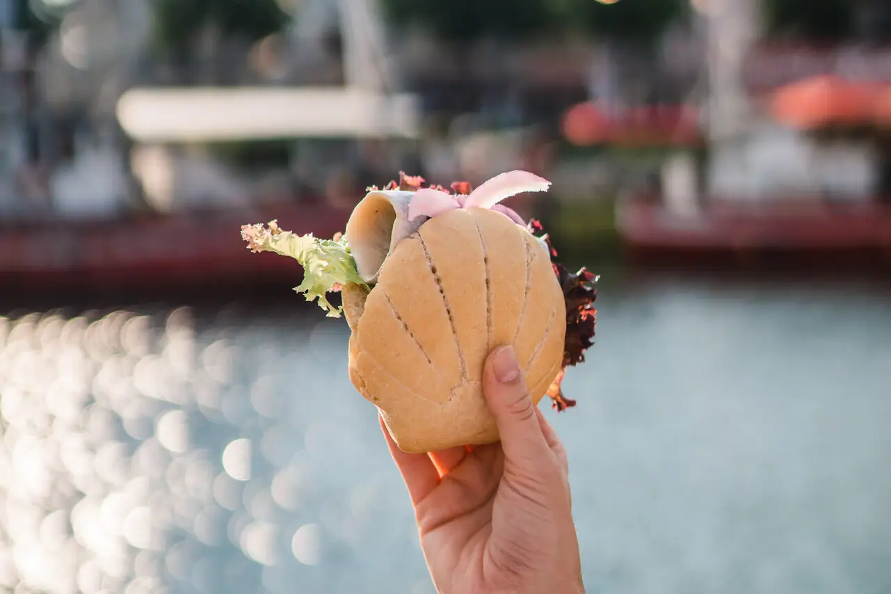 Eine Hand hält ein Fischbrötchen über glitzerndem Wasser.