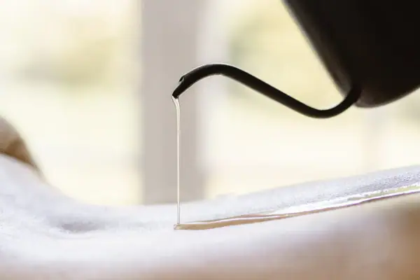 Quellfrische - Massage Eine Person gießt Öl auf den Rücken einer anderen Person.