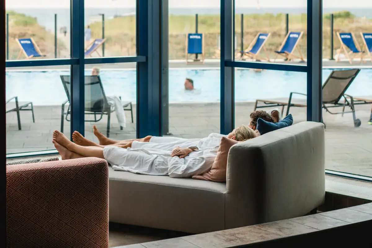 Ruhebereich im aja Warnemünde Eine Frau liegt auf einer Couch neben einem Pool.