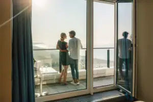 Suite im aja Warnemünde Ein Mann und eine Frau stehen auf einem Balkon mit Blick auf einen Strand.