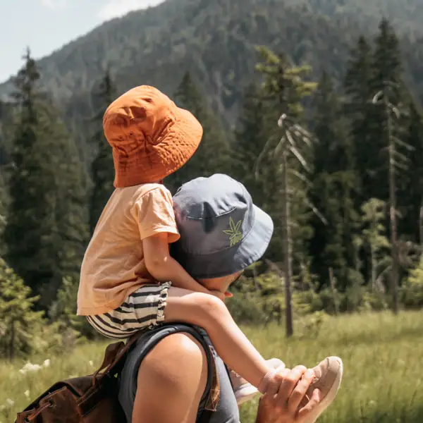 Vater und Kind Ein Mann trägt ein Kind auf seinen Schultern in einem Feld mit Bäumen und Bergen.