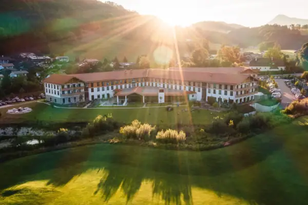 aja Ruhpolding Ein großes Gebäude mit einem großen Rasen und einem Parkplatz im Vordergrund.