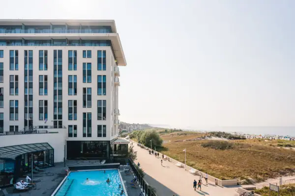 aja Warnemünde Ein Gebäude mit einem Pool und vorbeigehenden Menschen.