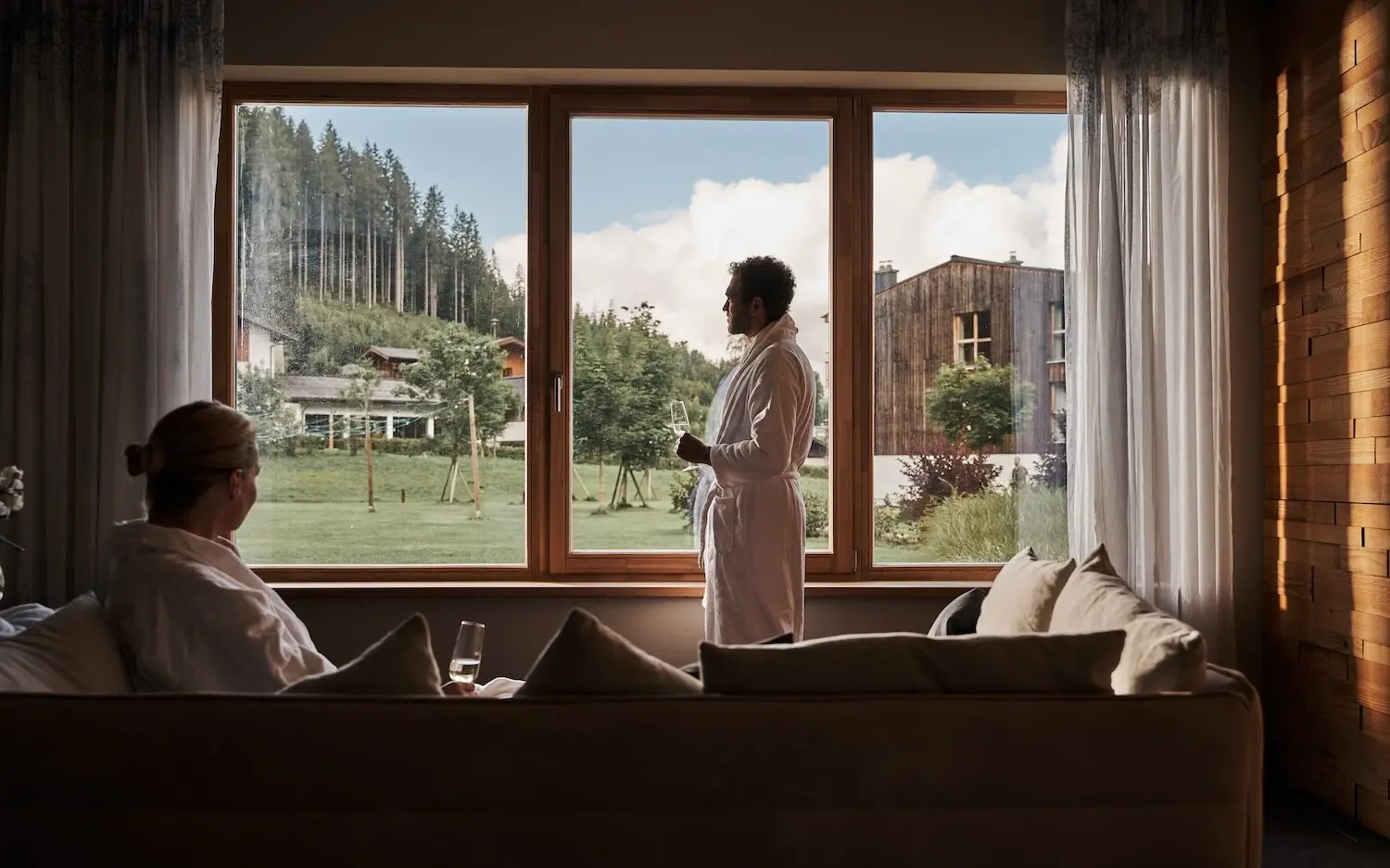 Wellness aja Werfenweng Mann in Bademantel steht in einem Wellnessbereich vor einem Fenster.