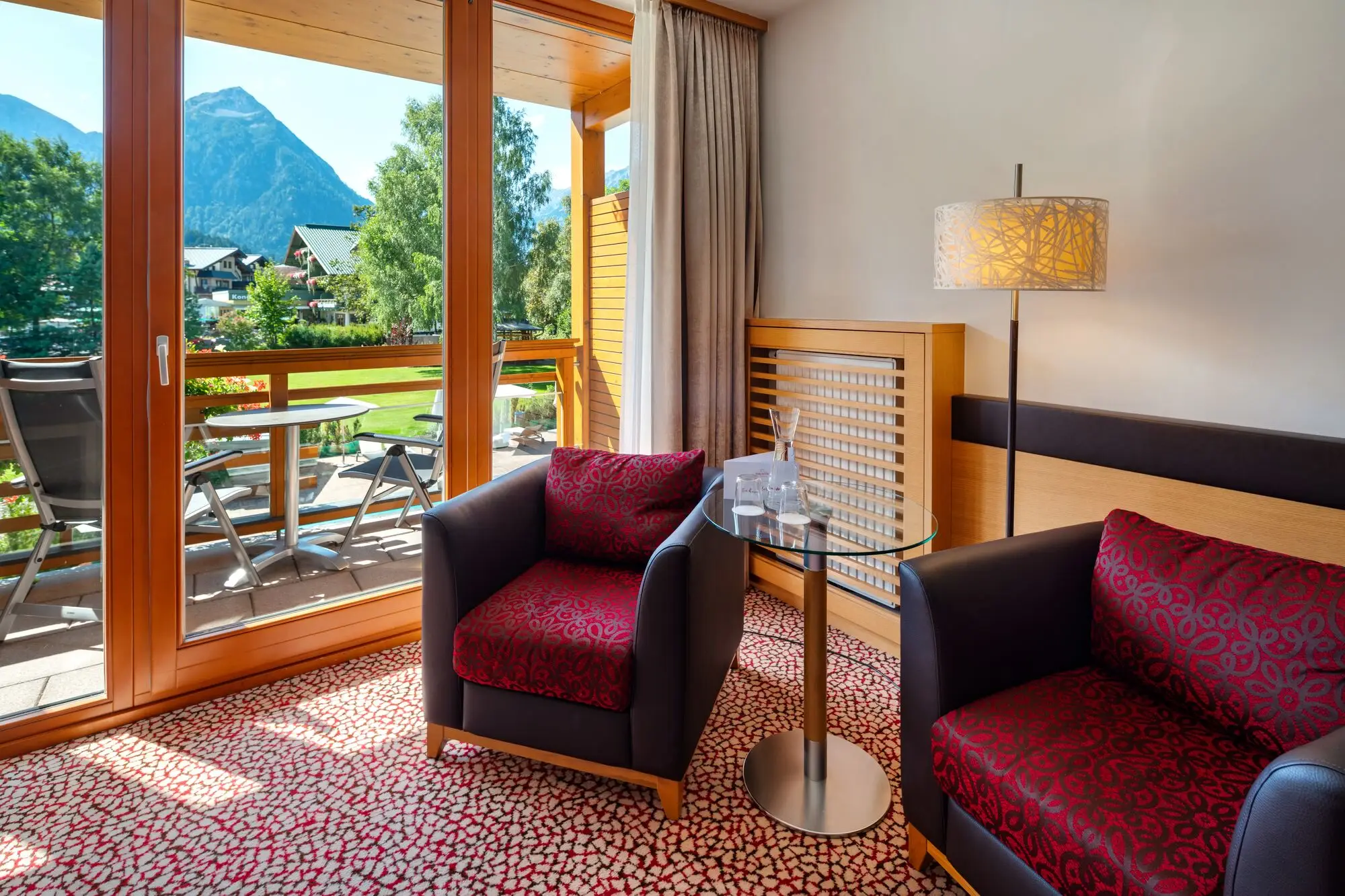 Zimmer aja Fürstenhaus am Achensee Innenraum mit zwei Sesseln und einem Tisch. Im Hintegrund ist Balkon zu sehen mit Blick auf die Berge.