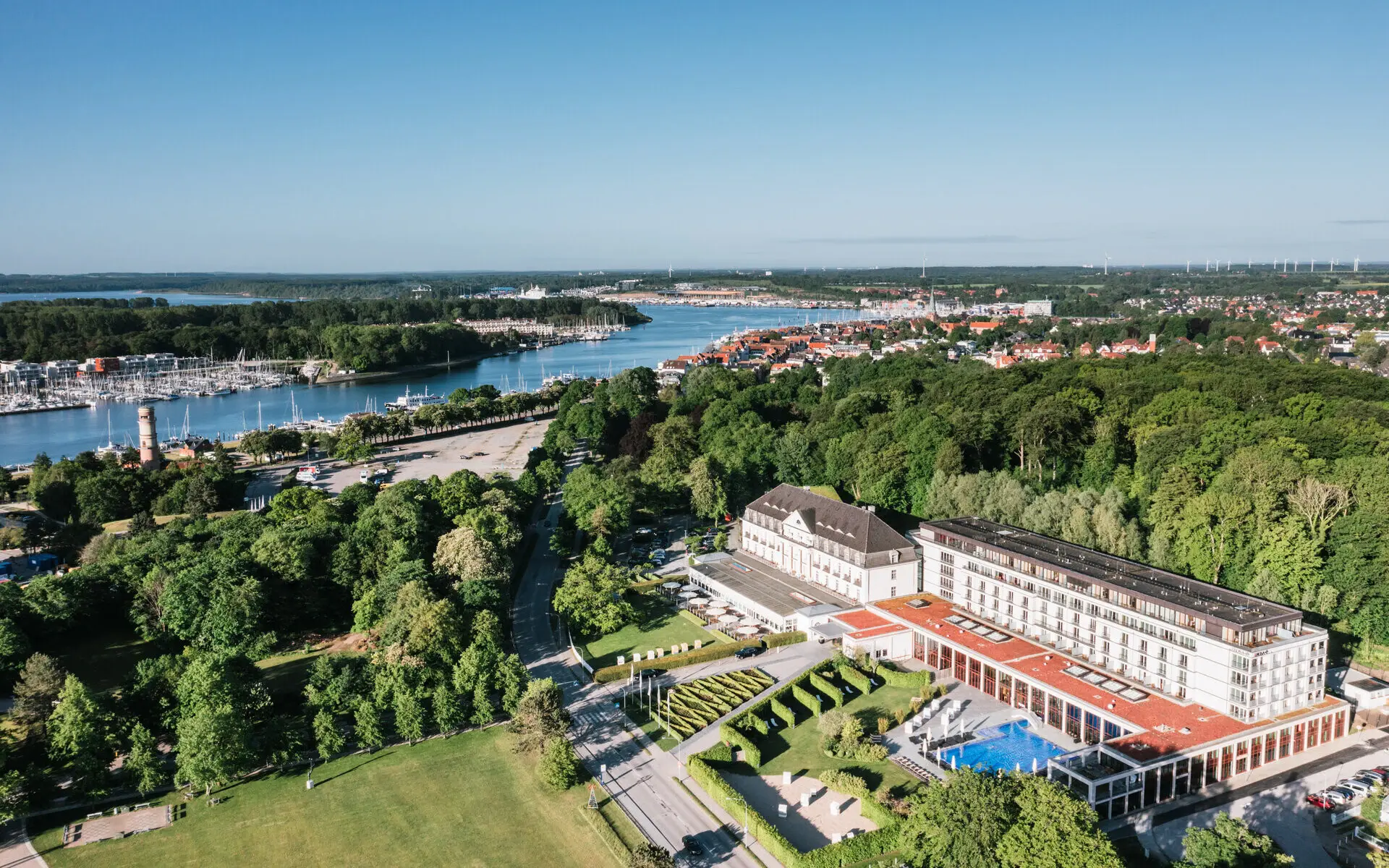 A-ROSA Travemünde Luftaufnahme des A-ROSA Travemünde, idyllisch gelegen an der Ostseeküste, umgeben von grünen Parkanlagen, mit Blick auf den Yachthafen, die Lübecker Bucht und die malerische Stadt Travemünde.