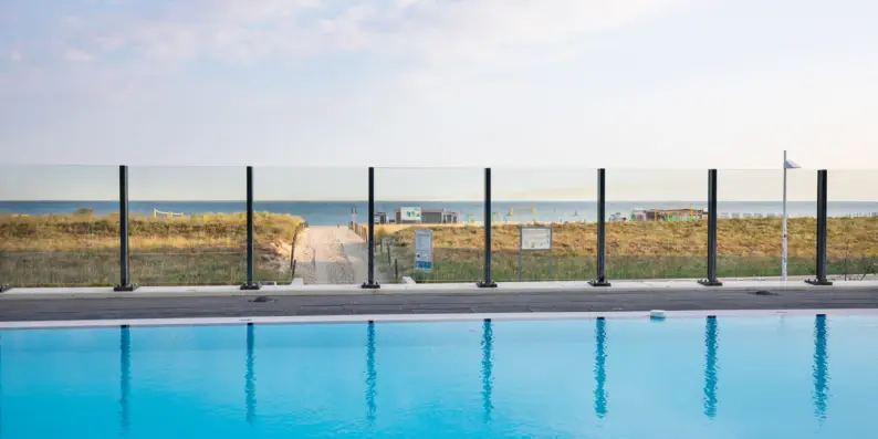Ein ruhiger Außenpool, umgeben von einer Glasmauer, mit direktem Blick auf die Dünen und den Strand an einem sonnigen Tag. Ein ruhiger Außenpool, umgeben von einer Glasmauer, mit direktem Blick auf die Dünen und den Strand an einem sonnigen Tag.