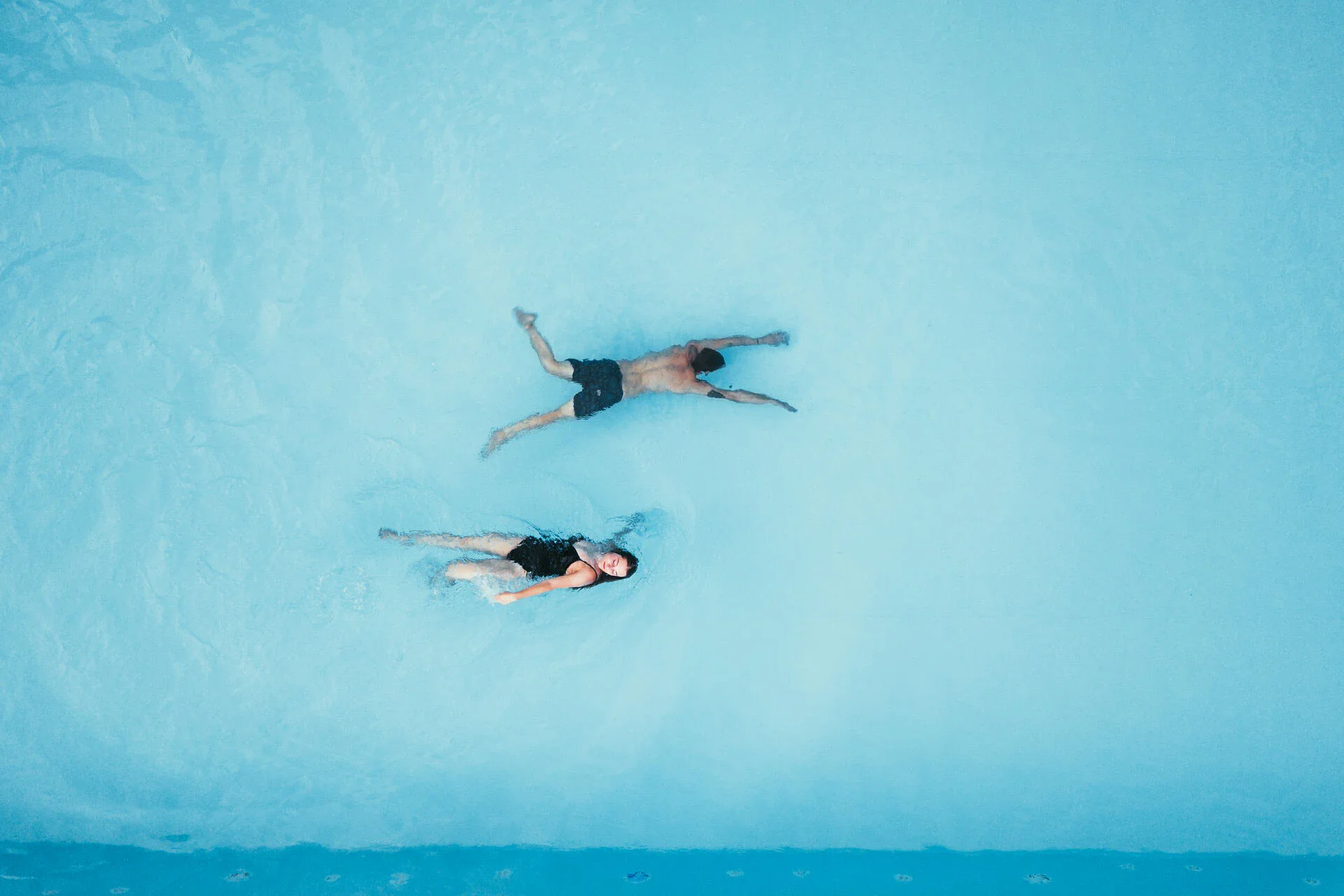 Seebad Zwei Personen schwimmen in hellblauem Wasser. Die Frau in schwarzem Badeanzug schwimmt auf ihrem Rücken und der Mann auf seinem Bauch.