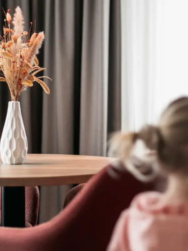 Suite Ein Mädchen sitzt an einem Tisch mit einer Blumenvase.