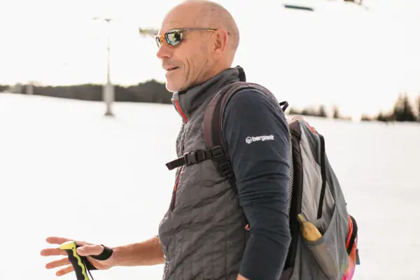 Tourguide Ein Mann mit Sonnenbrille und Rucksack geht auf Schnee.