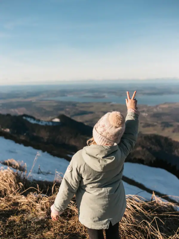 Kleines Mädchen Eine Person steht auf einem Hügel und zeigt ein Peace-Zeichen.