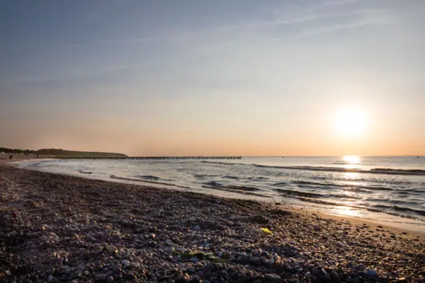 Strand Strand mit Felsen, Wasser und einem Pier im Hintergrund.