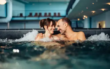 Ein Paar sitzt lächelnd im sprudelnden Whirlpool.