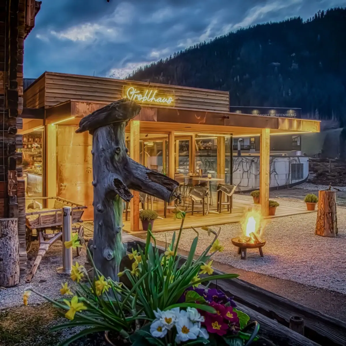 Das Gebäude von vorne mit einer Feuerstelle und einem Baumstumpf davor.