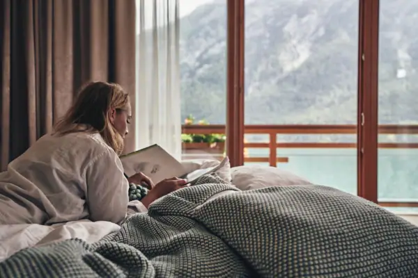 Zimmer mit Seeblick im aja Fürstenhaus am Achensee Eine Frau liegt auf einem Bett und liest ein Buch.