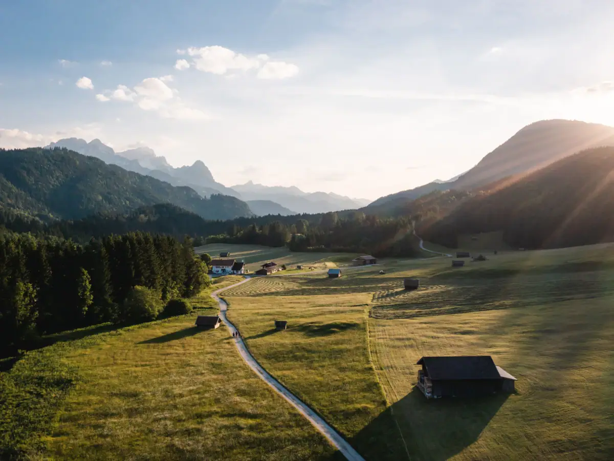 Landschaft mit Bergen Grünes Feld mit Gebäuden und Bäumen im Hintergrund.