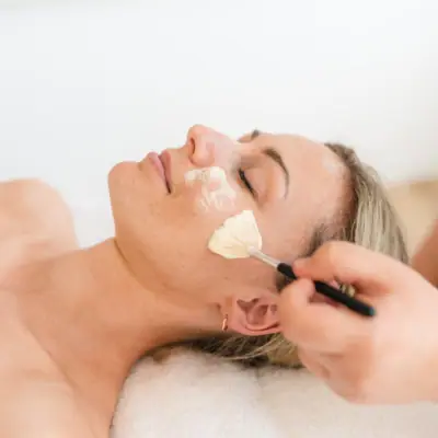 Gesichtsbehandlung Eine Frau liegt bei ander Anwendung auf dem Rücken mit einem Pinsel auf ihrem Gesicht.