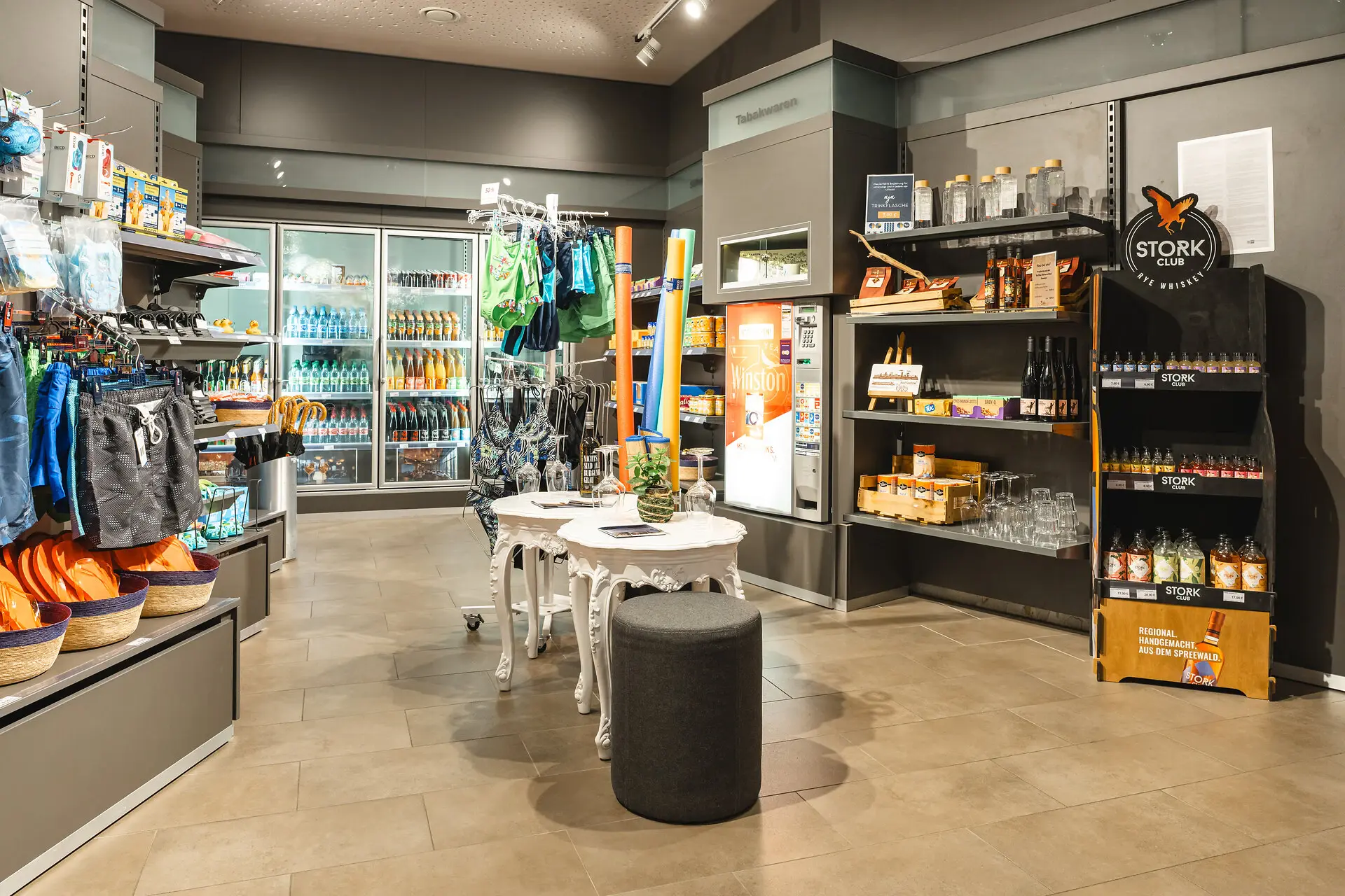 Shop aja Bad Saarow Der Shop im aja Bad Saarow mit kühlen Getränken, Badesachen und Snacks in einem grau gestrichenen Raum mit angenehmem Licht.