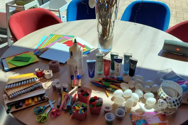 Osterbasteln Ein Tisch mit Kunstbedarf und einer Vase mit Blumen.