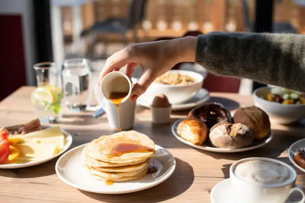 Pancakes Eine Person gießt Sirup auf einen Stapel Pfannkuchen.